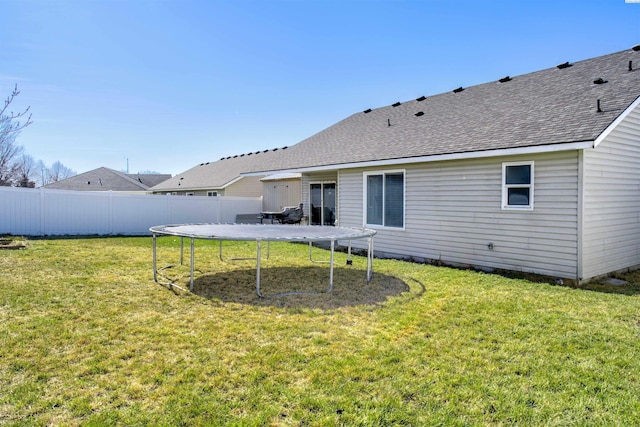 back of property with a shingled roof, a trampoline, fence, and a lawn