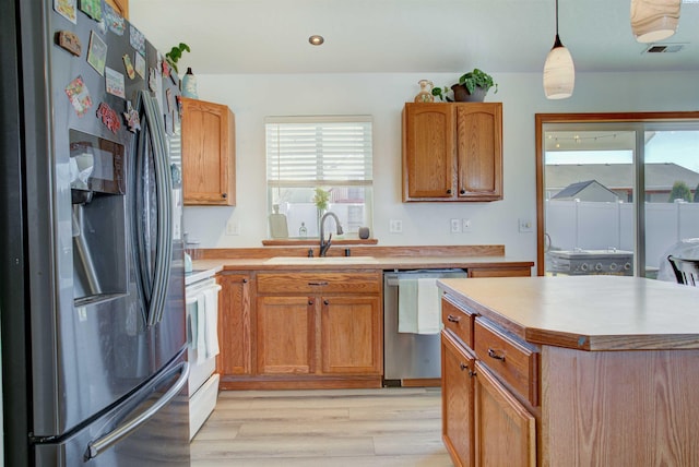 kitchen featuring light wood finished floors, light countertops, appliances with stainless steel finishes, and a sink