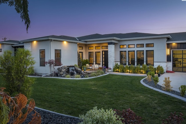 975 Rieve Ct, Richland, WA 99352 - back of house at dusk featuring a lawn, stucco siding, stone siding, and a garage