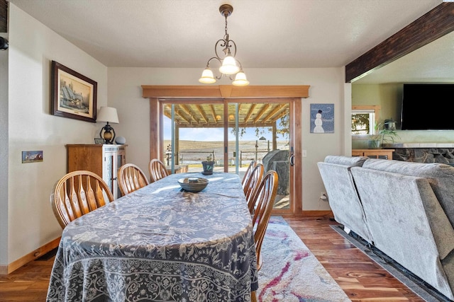 dining space featuring a chandelier, beamed ceiling, baseboards, and wood finished floors