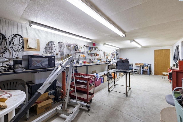 miscellaneous room with wallpapered walls, a workshop area, concrete floors, and a textured ceiling