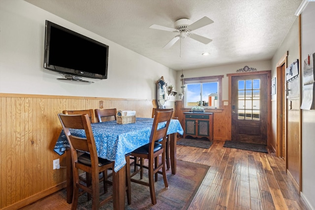 dining space with wooden walls, wainscoting, ceiling fan, hardwood / wood-style flooring, and a textured ceiling