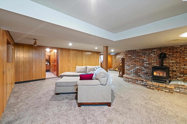 living room featuring carpet floors, a wood stove, recessed lighting, stairs, and wood walls