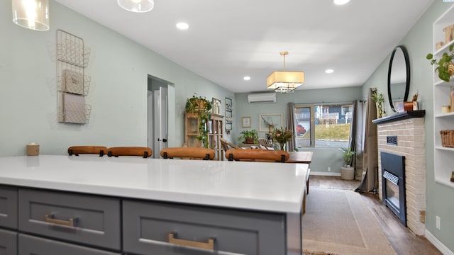 kitchen featuring decorative light fixtures, light countertops, gray cabinetry, a brick fireplace, and a wall mounted air conditioner