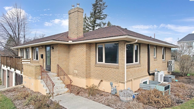 exterior space with ac unit, brick siding, a chimney, a shingled roof, and fence