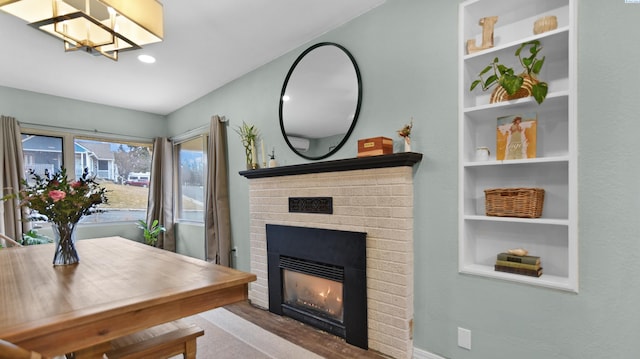 dining area with a brick fireplace, built in features, and wood finished floors