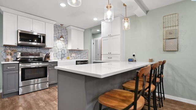 kitchen featuring light countertops, appliances with stainless steel finishes, gray cabinets, and a kitchen breakfast bar