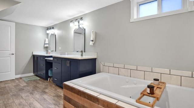 bathroom with a garden tub, a sink, wood finished floors, baseboards, and double vanity