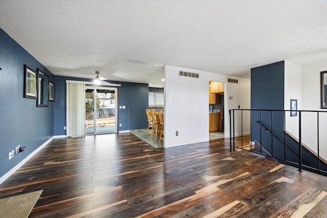 empty room with baseboards, visible vents, a ceiling fan, dark wood-style flooring, and a textured ceiling