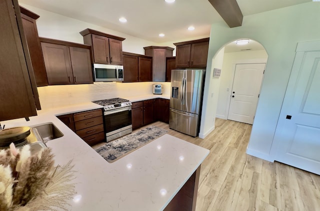4516 NW Commons Dr, Pasco, WA 99301 - kitchen with stainless steel appliances, light wood finished floors, dark brown cabinets, arched walkways, and tasteful backsplash