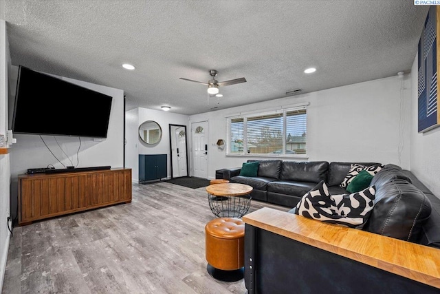 living room featuring hardwood / wood-style flooring, ceiling fan, and a textured ceiling