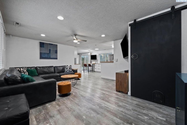 living room with hardwood / wood-style flooring, ceiling fan, a barn door, and a textured ceiling