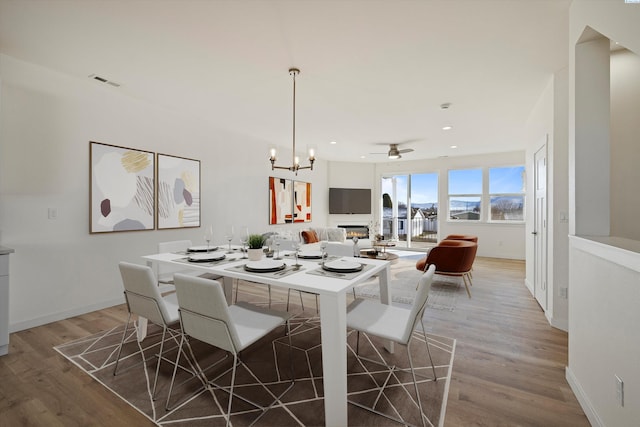 125 Claret Dr, Prosser, WA 99350 - dining space with visible vents, baseboards, light wood-type flooring, ceiling fan with notable chandelier, and a glass covered fireplace