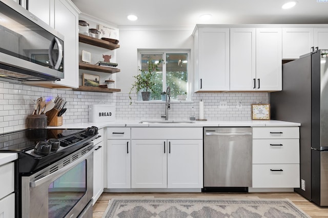 kitchen with sink, light hardwood / wood-style flooring, appliances with stainless steel finishes, white cabinetry, and tasteful backsplash