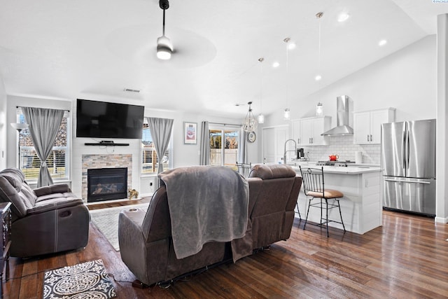 living room with sink, dark wood-type flooring, ceiling fan, high vaulted ceiling, and a fireplace