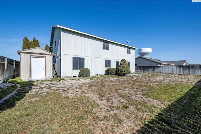 rear view of house with a storage shed, a yard, an outdoor structure, and fence