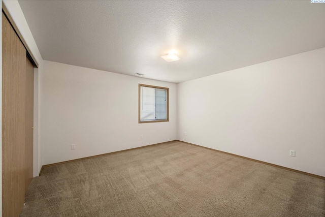 unfurnished room with visible vents, baseboards, a textured ceiling, and light colored carpet