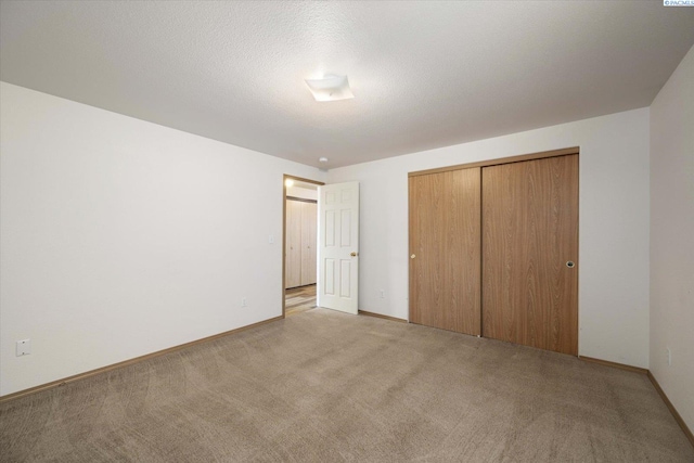 unfurnished bedroom with a closet, light carpet, a textured ceiling, and baseboards