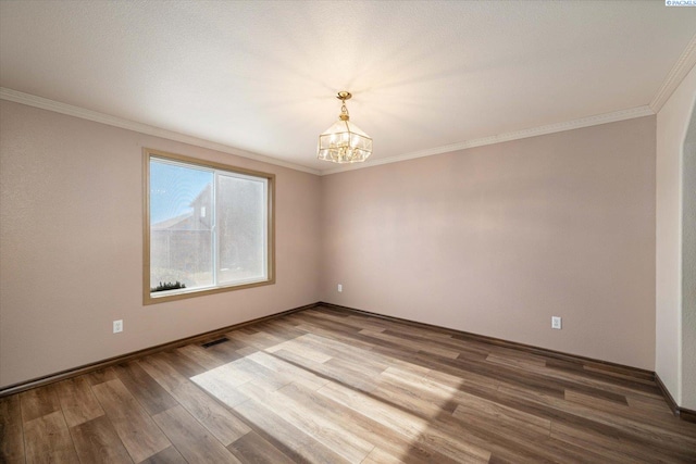 unfurnished room featuring a notable chandelier, wood finished floors, visible vents, and crown molding