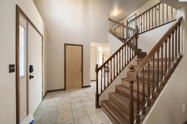 foyer entrance featuring a towering ceiling, light tile patterned floors, and baseboards