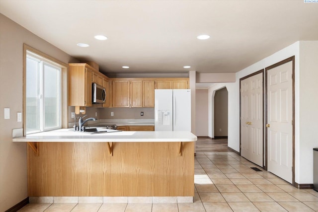 kitchen with white refrigerator with ice dispenser, arched walkways, stainless steel microwave, light countertops, and a sink