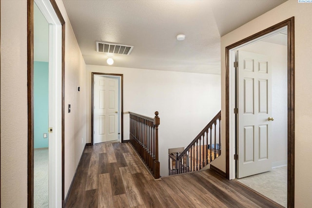 hallway with baseboards, visible vents, wood finished floors, and an upstairs landing