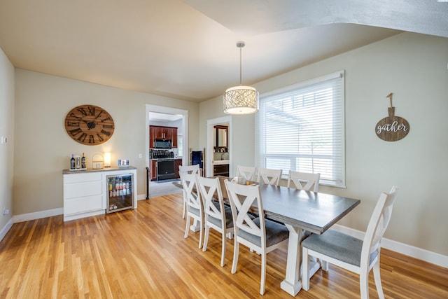 dining area featuring beverage cooler, light wood finished floors, a dry bar, and baseboards