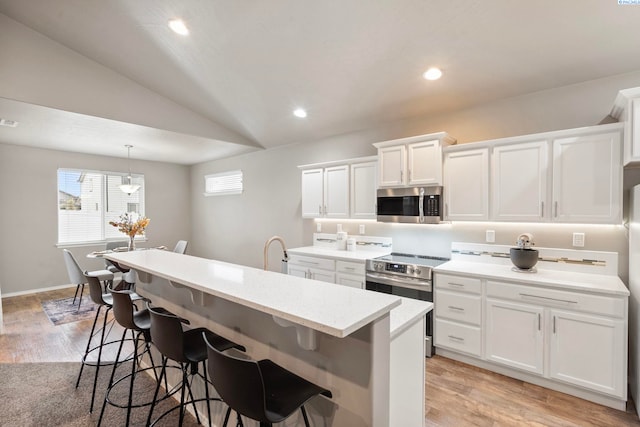 kitchen with appliances with stainless steel finishes, white cabinetry, hanging light fixtures, a center island with sink, and vaulted ceiling