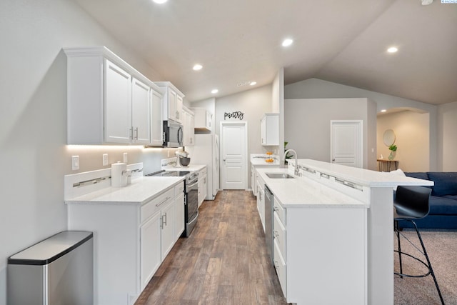 kitchen featuring sink, appliances with stainless steel finishes, white cabinetry, a kitchen bar, and vaulted ceiling