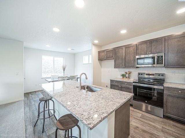 kitchen with sink, a center island with sink, appliances with stainless steel finishes, a kitchen breakfast bar, and backsplash