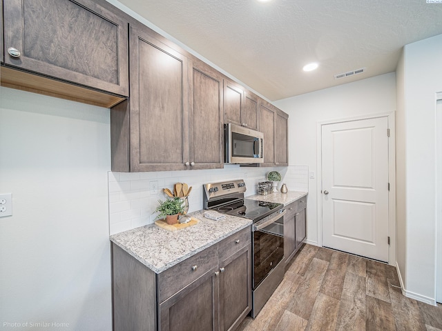 kitchen with tasteful backsplash, light hardwood / wood-style floors, stainless steel appliances, light stone countertops, and dark brown cabinets