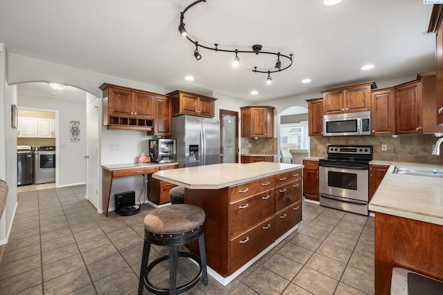 kitchen featuring a sink, stainless steel appliances, a center island, arched walkways, and washer and clothes dryer