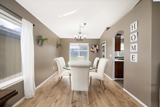 dining room with light wood-style floors, a notable chandelier, vaulted ceiling, and arched walkways