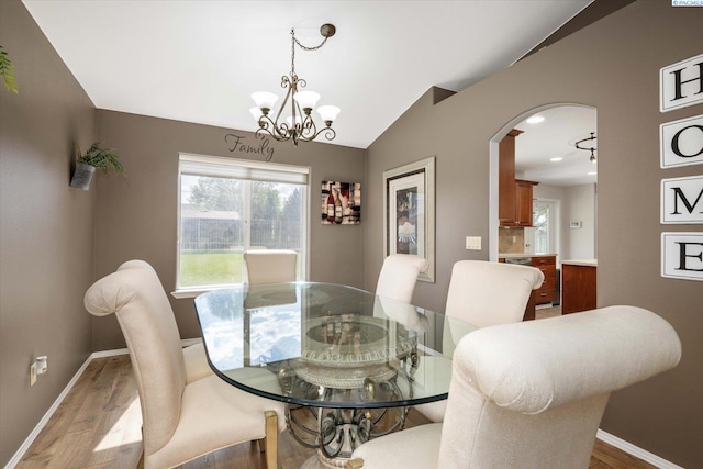 dining area featuring wood finished floors, baseboards, a notable chandelier, and arched walkways