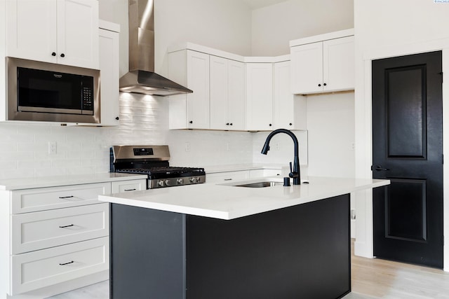 kitchen featuring stainless steel range oven, wall chimney range hood, light countertops, built in microwave, and a center island with sink