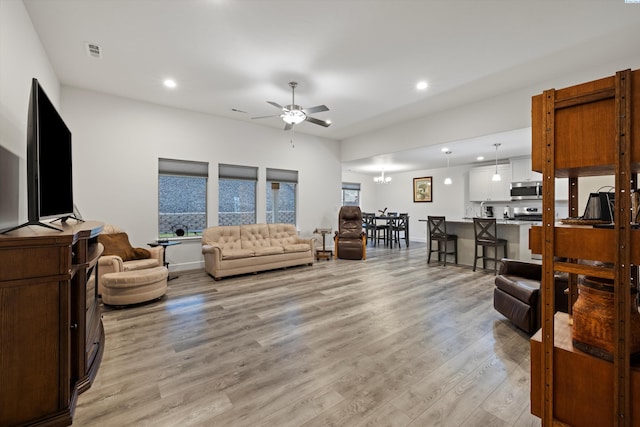 living room featuring ceiling fan with notable chandelier and light wood-type flooring