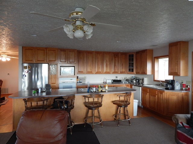kitchen with white appliances, brown cabinets, ceiling fan, and a sink