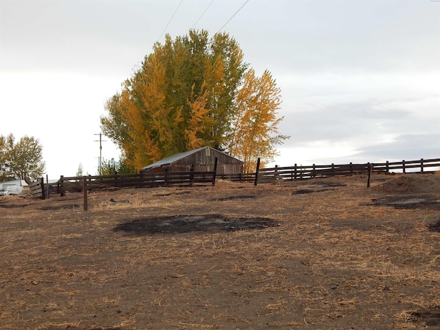 view of yard featuring an outdoor structure, a rural view, and fence