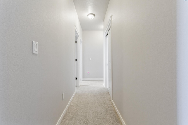 corridor with baseboards and light carpet