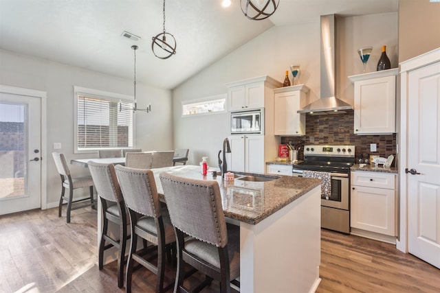 kitchen featuring visible vents, a center island with sink, a sink, stainless steel appliances, and wall chimney exhaust hood