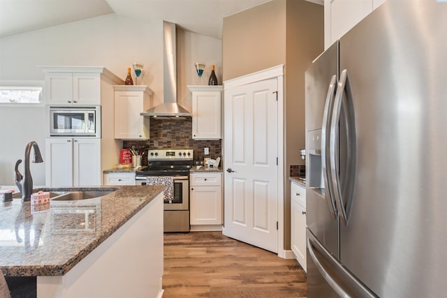 kitchen with wall chimney range hood, appliances with stainless steel finishes, wood finished floors, white cabinets, and a sink