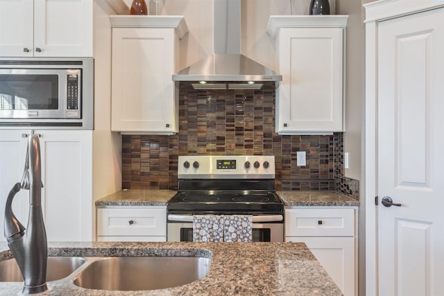 kitchen featuring wall chimney range hood, decorative backsplash, appliances with stainless steel finishes, white cabinetry, and a sink