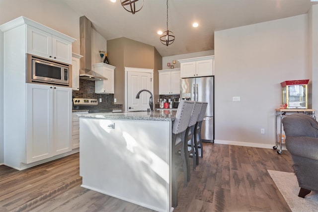 kitchen featuring tasteful backsplash, dark wood-type flooring, appliances with stainless steel finishes, white cabinetry, and wall chimney exhaust hood