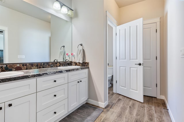 full bath with double vanity, toilet, wood finished floors, and a sink