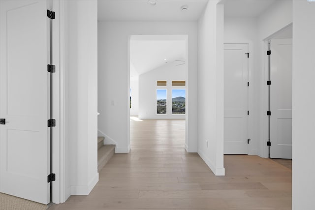 hallway with vaulted ceiling and light wood-type flooring