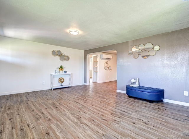 empty room with hardwood / wood-style flooring, an AC wall unit, and a textured ceiling