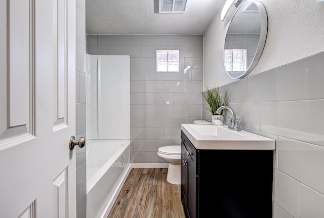 full bathroom with toilet, wood-type flooring, tub / shower combination, tile walls, and vanity