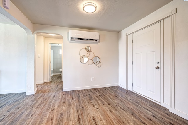 empty room featuring a wall mounted AC, a textured ceiling, and light wood-type flooring