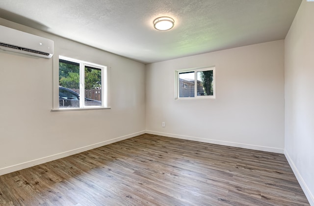 spare room with hardwood / wood-style flooring, plenty of natural light, an AC wall unit, and a textured ceiling