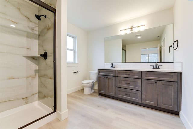 full bath featuring wood finished floors, a marble finish shower, toilet, double vanity, and baseboards